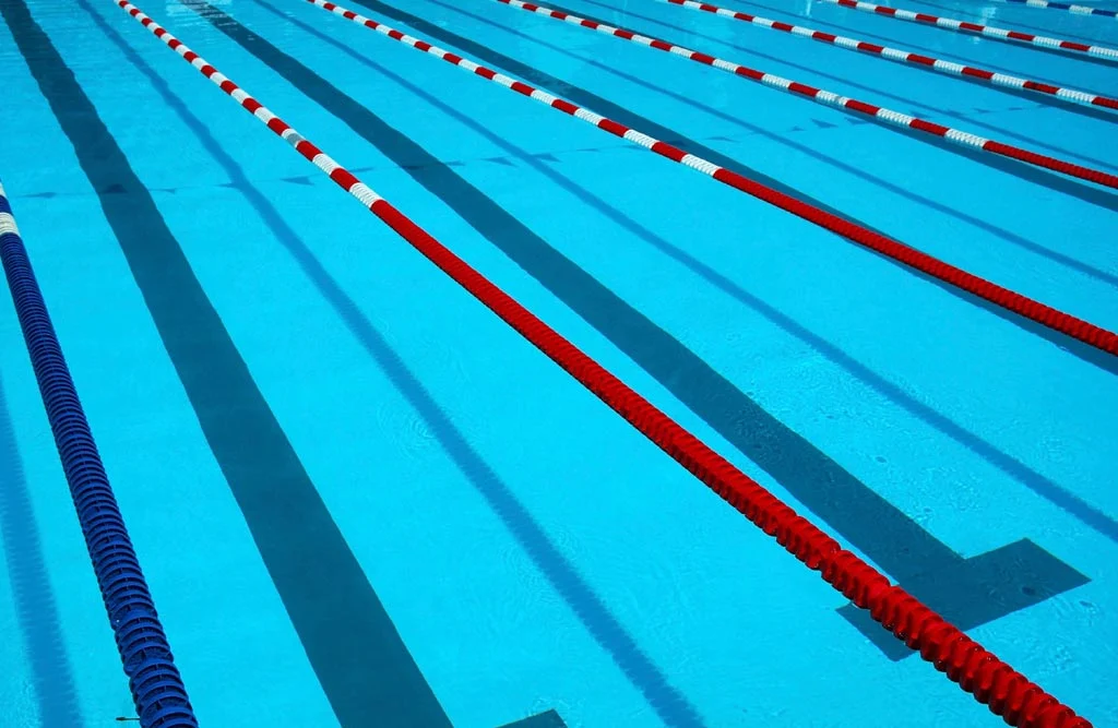 A swimming pool starting block marked with the number four sits at the edge of a lane with blue and yellow lane markers.